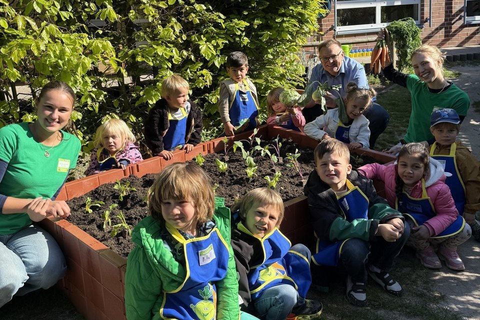 Das Foto zeigt die Kinder und Erwachsenen, die rund um das bepflanzte Hochbeet hocken.