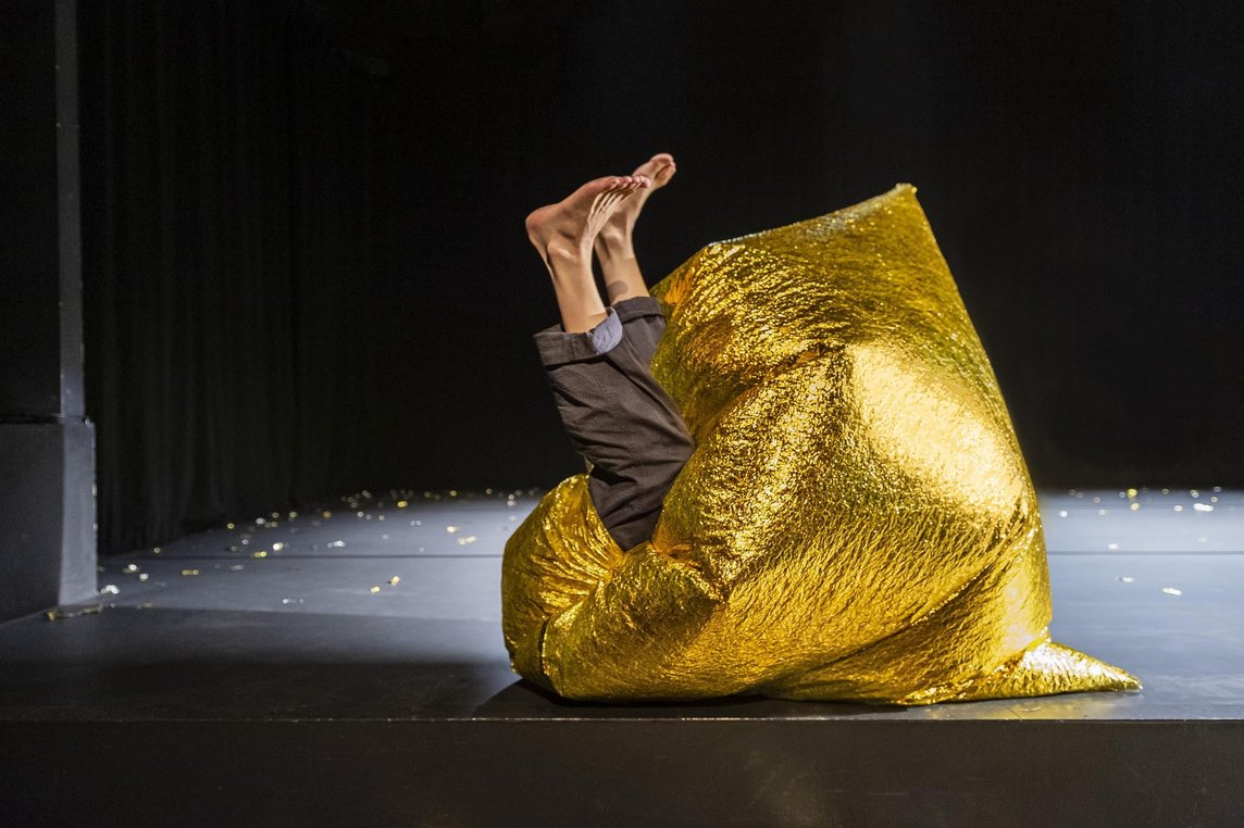 Das Foto zeigt einen goldenen Sack, aus dem zwei Beine herausschauen.