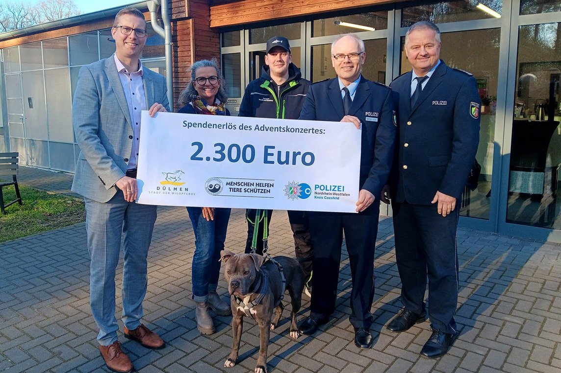 Das Bild zeigt insgesamt fünf Personen, die einen Spendenscheck hochhalten. Vor den Personen steht ein Hund 